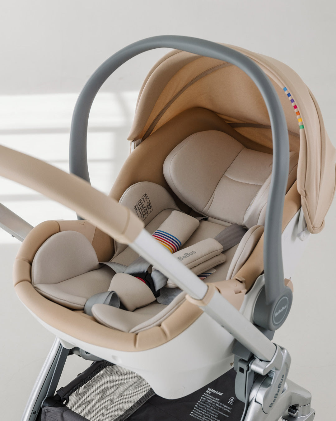 BeBeBus Guard Infant Car Seat attached to a stroller frame in a bright, minimalist room, showcasing the padded insert and canopy.