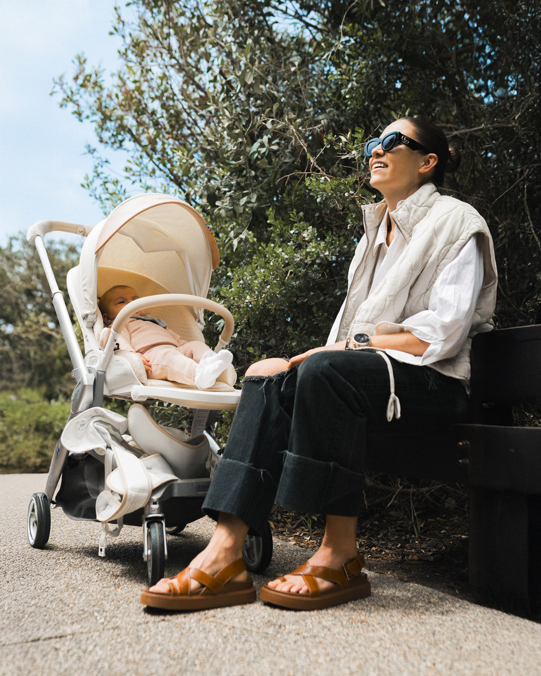 Stylish mom smiles beside the BeBeBus Art+ PRO Stroller on a nature walk, showcasing a luxury compact baby stroller for newborns and toddlers.