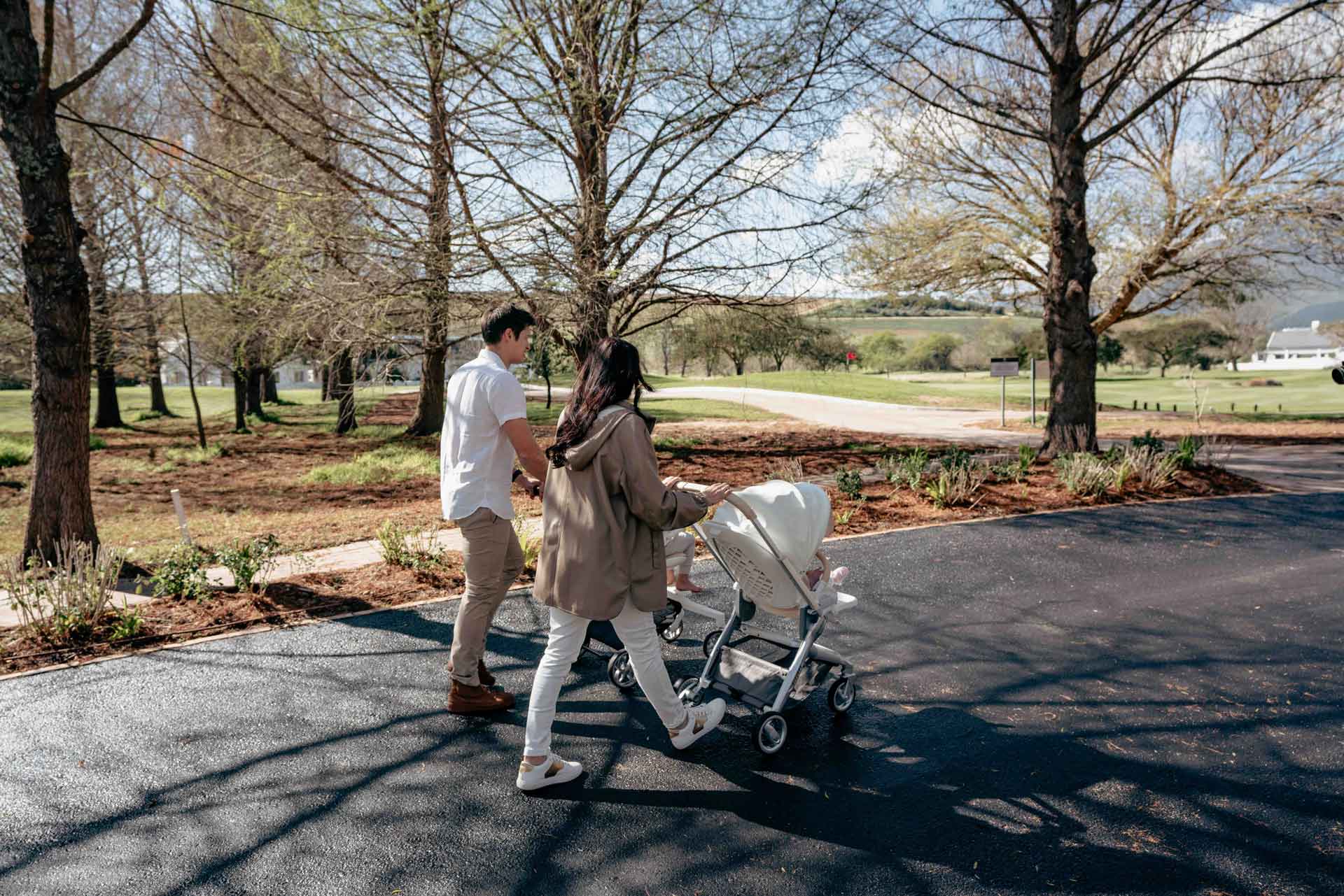 Two people pushing a BeBeBus stroller in a park setting with trees and open space.
