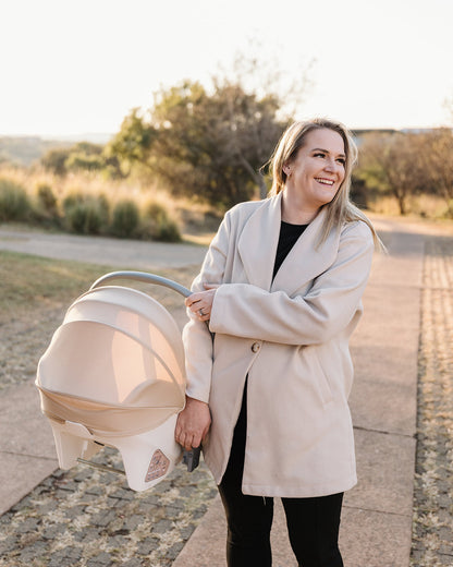 Woman smiling while carrying the BeBeBus Guard Car Seat by its handle during a walk outdoors.