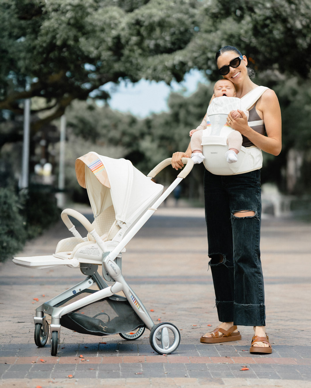 Mother pushing an Art + stroller and holding her baby in the BeBEBus carrier outdoors.