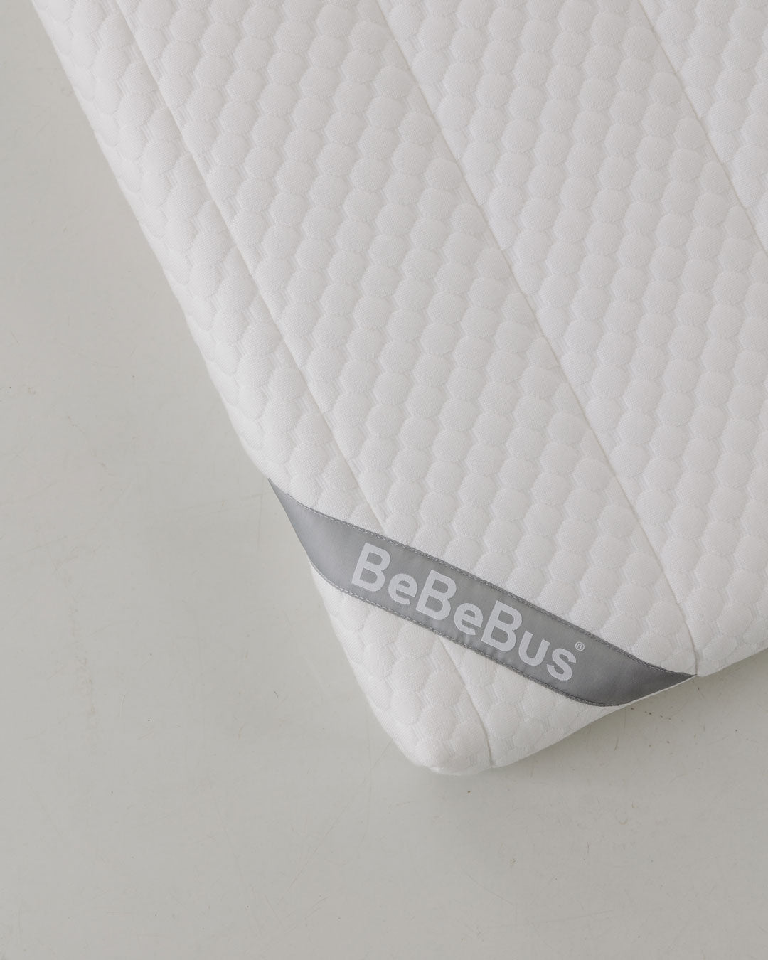 Close-up of the BeBeBus baby mattress corner with soft quilted texture and branded tag.