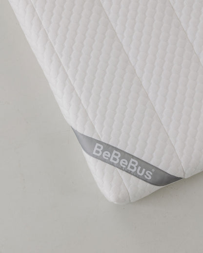 Close-up of the BeBeBus baby mattress corner with soft quilted texture and branded tag.