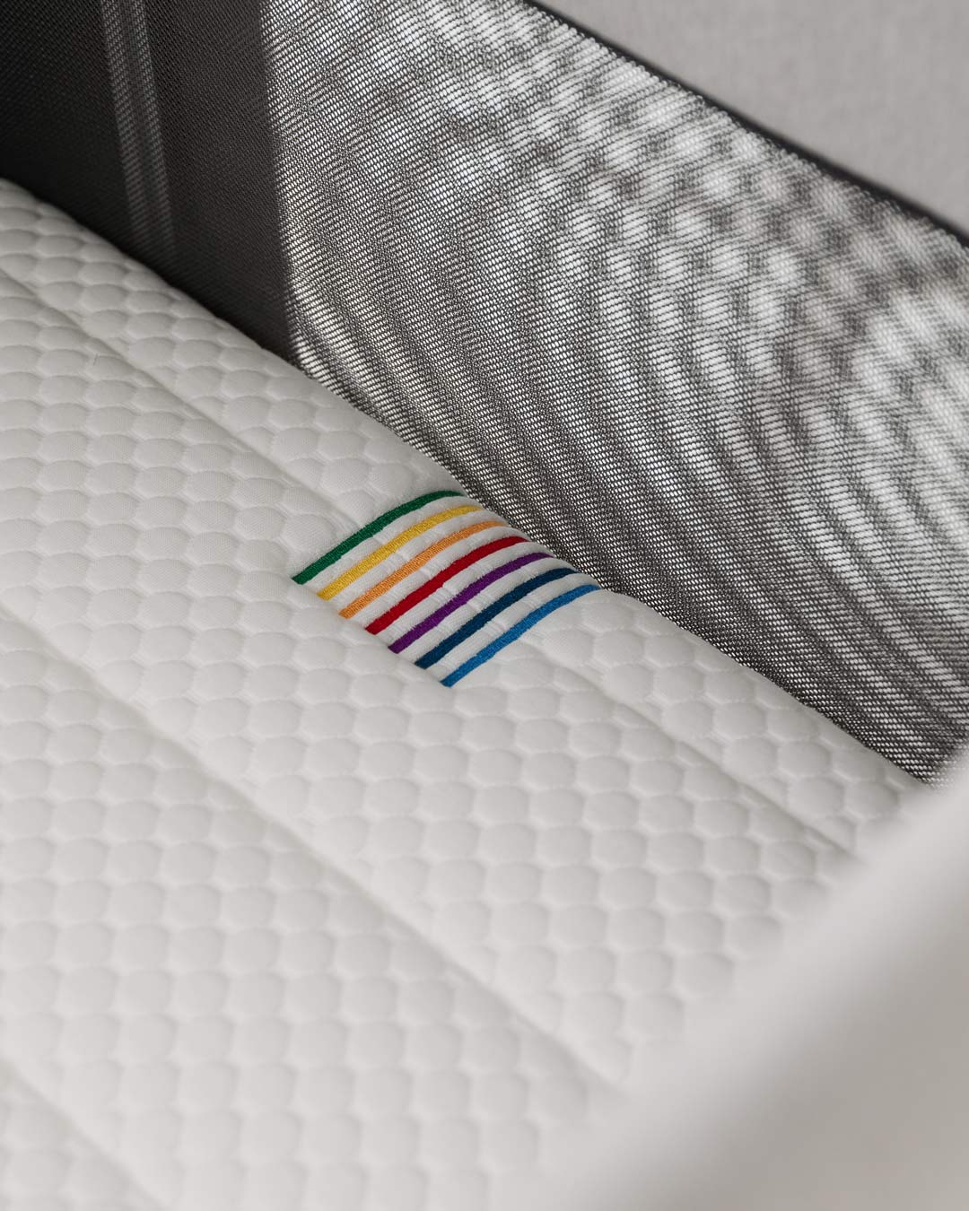 Quilted BeBeBus mattress detail inside crib with breathable mesh sides and rainbow stitching.