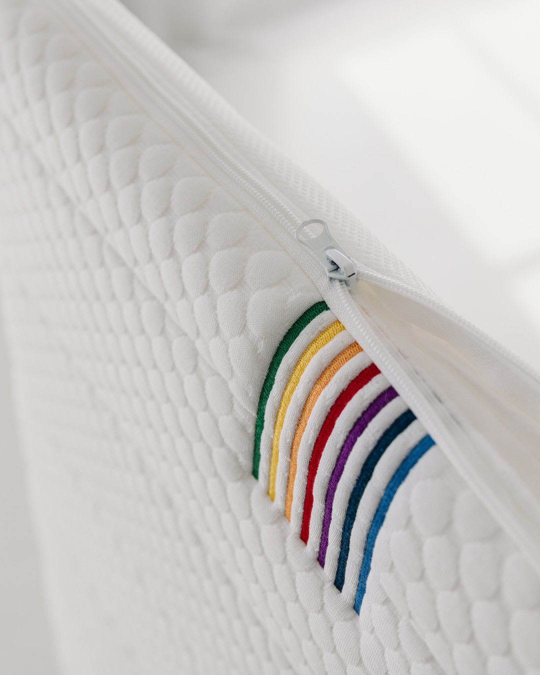 Side view of the BeBeBus baby mattress showing removable zip cover with colourful stitched detailing.