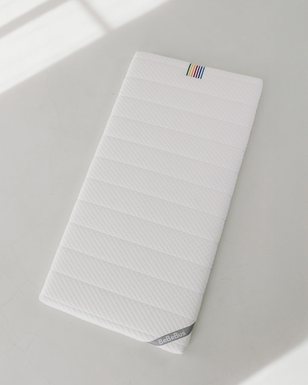 Full view of BeBeBus newborn-to-toddler mattress on a clean white surface, showcasing its flat, breathable design.