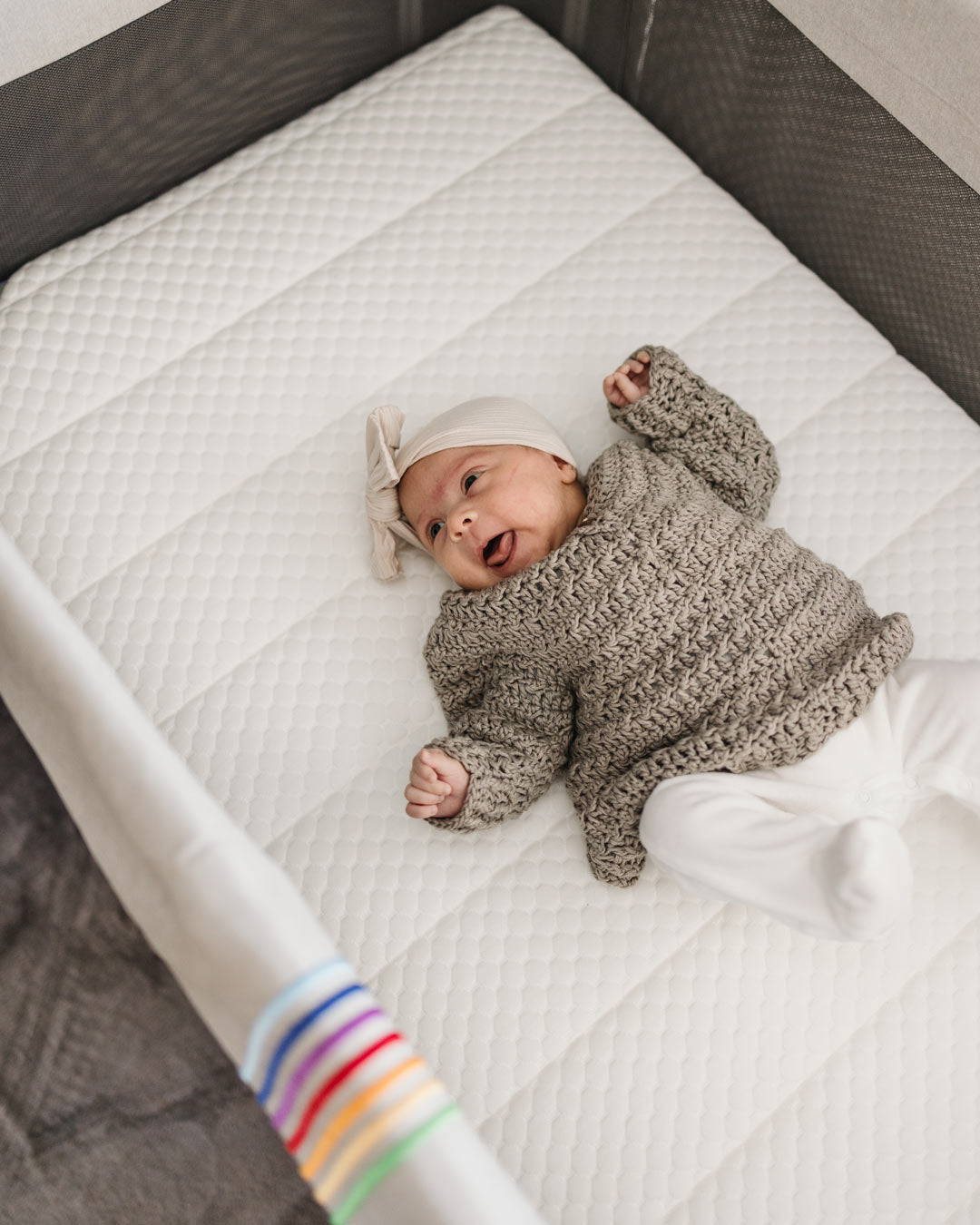 Newborn baby resting on BeBeBus mattress inside crib, demonstrating comfort and support for safe sleep.