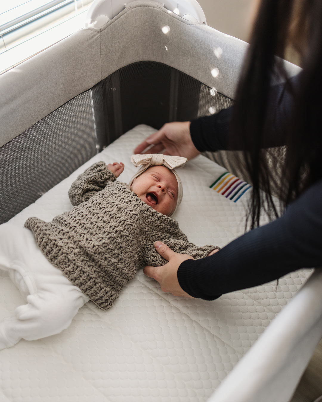 Happy baby lying comfortably in the BeBeBus Wish Crib, showcasing the soft, supportive mattress and safe, spacious sleep area.
