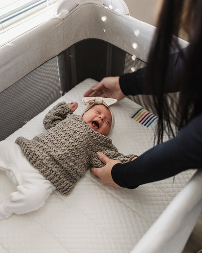 Happy baby lying comfortably in the BeBeBus Wish Crib, showcasing the soft, supportive mattress and safe, spacious sleep area.